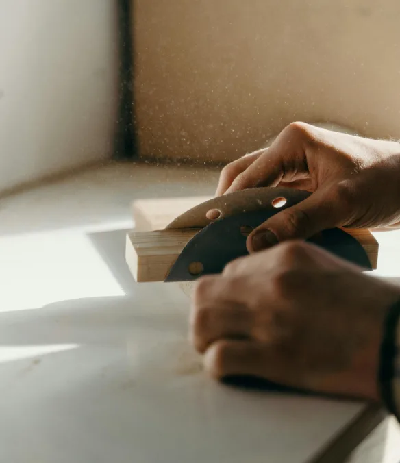 Hands sanding a timber block on a benchtop
